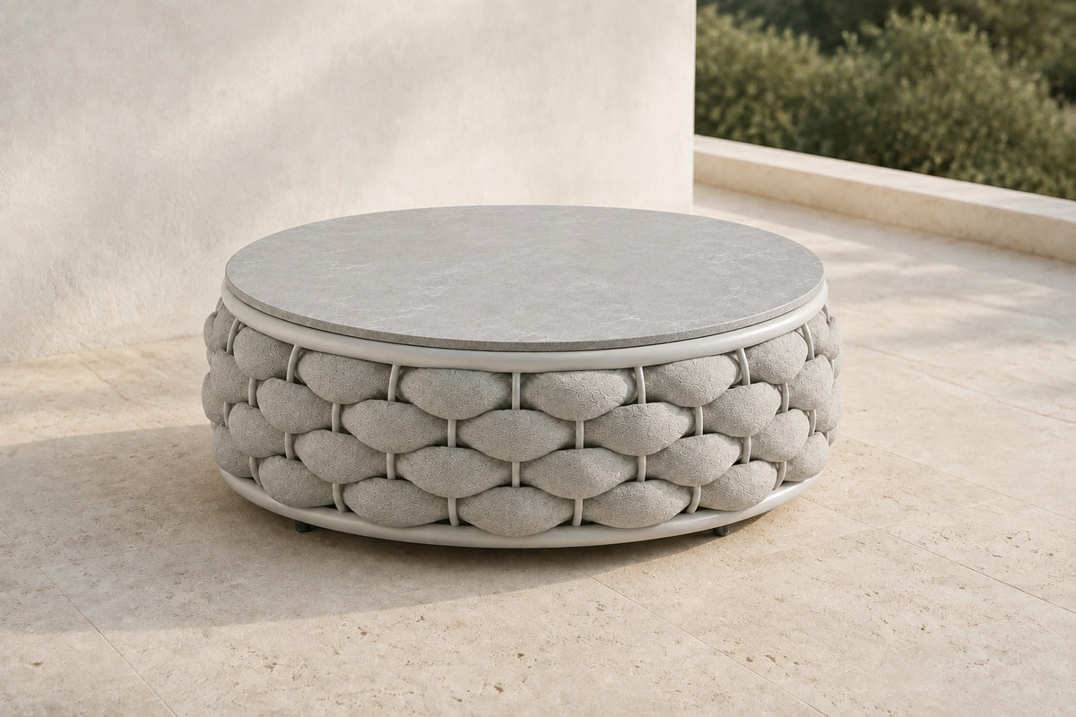 Cala round coffee table with grey hard top and chunky pale rope base, photographed on a travertine terrace