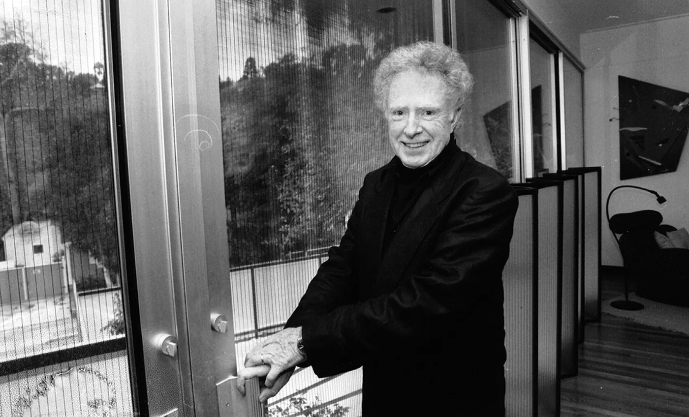 Portrait of architect Pierre Koenig, smiling beside a glass door