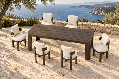 Lifestyle view: Serein aluminium dining table and six chairs on a coastal stone terrace