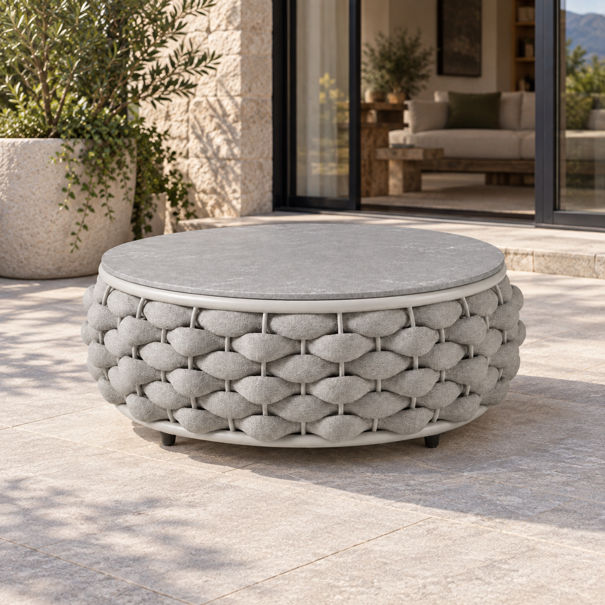 Lifestyle view: Cala round coffee table with grey hard top and chunky pale rope base, photographed in a limestone courtyard