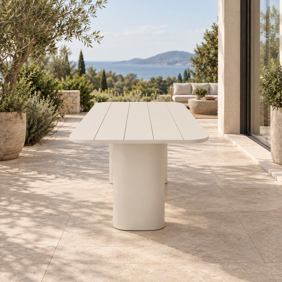 Lifestyle view: Ripple Dining Table in Aluminium, straight short-end view beside a coastal home