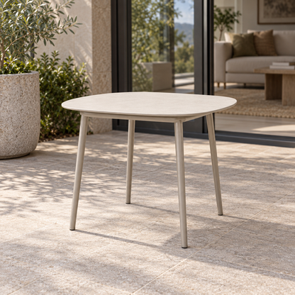 Lifestyle view: Tavira compact ivory coffee table on a pale grey metal base, photographed in a limestone courtyard