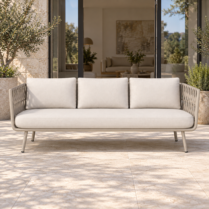 Lifestyle view: Tavira sofa with broad taupe straps, one ivory seat and three back cushions, photographed in a limestone courtyard